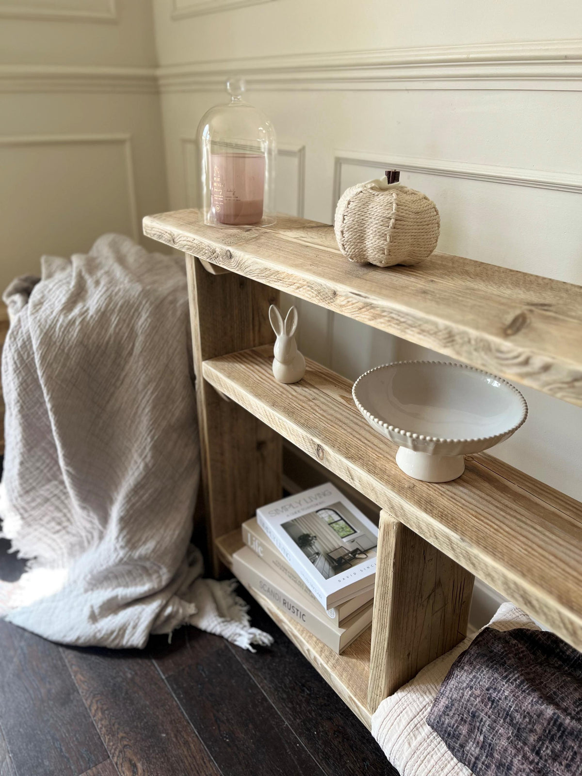 A farmhouse style wooden slim console table with one long shelf and two lower bottom shelves, in a living room setting (front view)