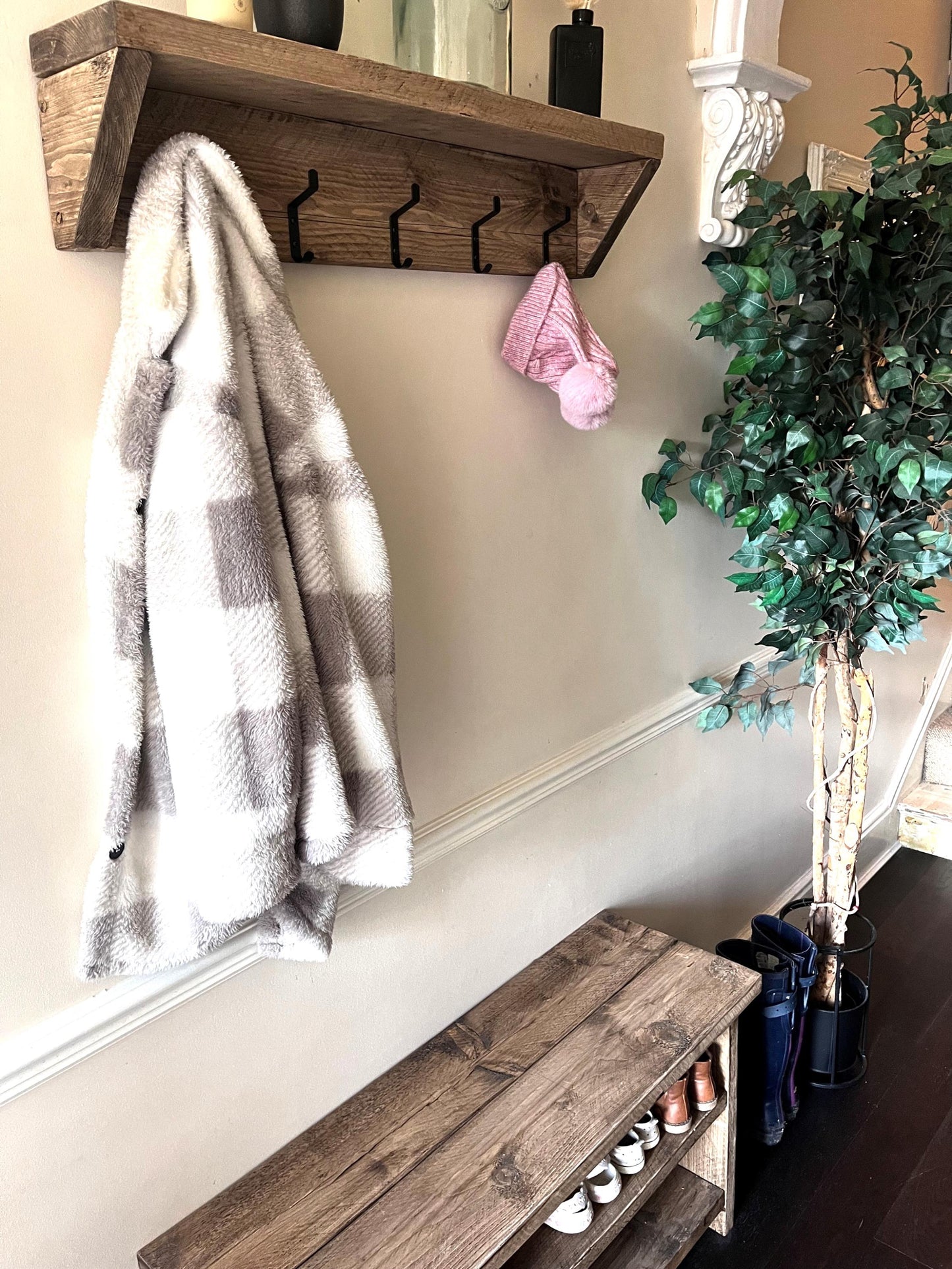Farmhouse style wooden coat rack with coat hooks, plaid blanket, and bench in a hallway setting.