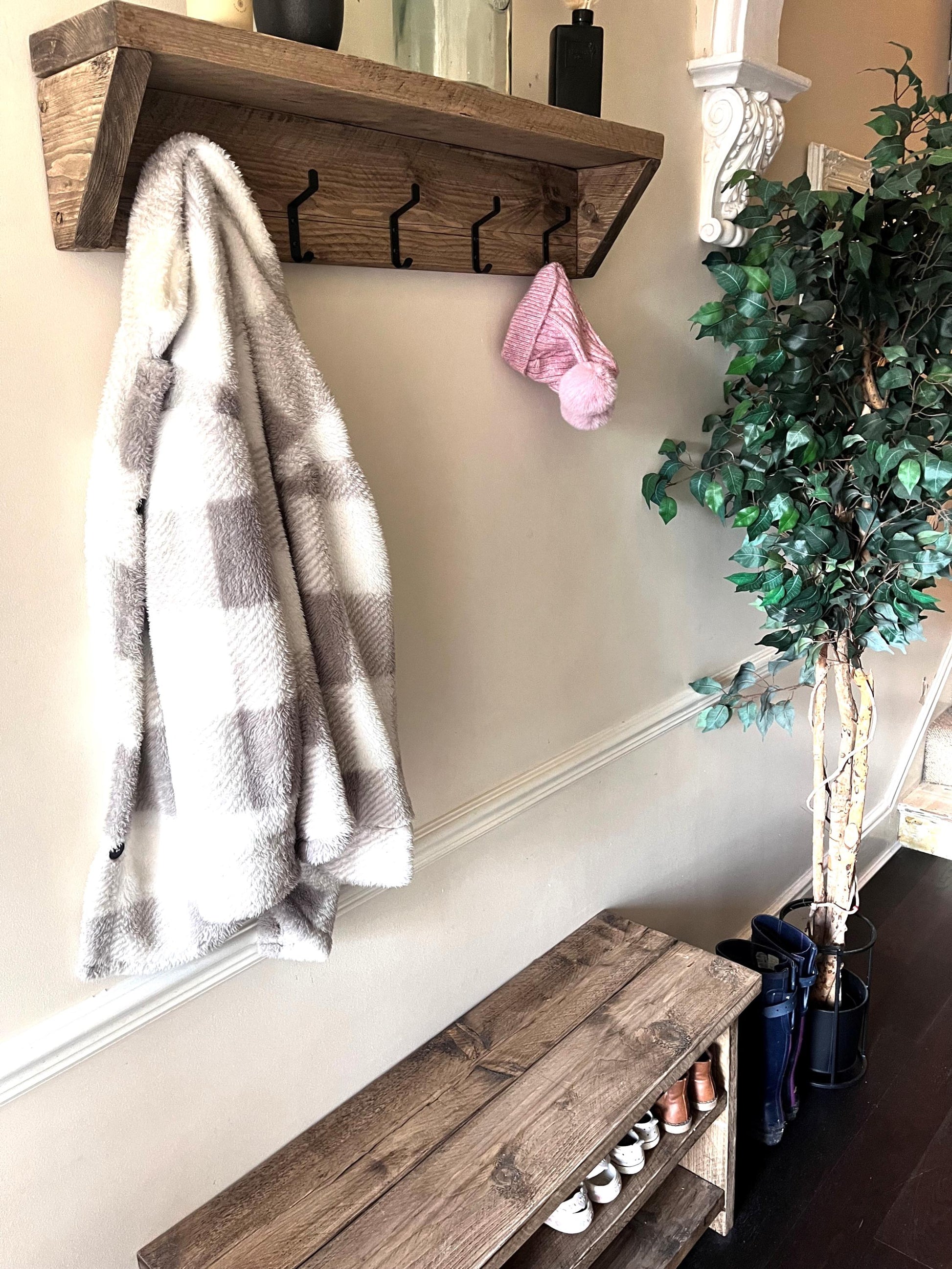 Farmhouse style wooden coat rack with coat hooks, plaid blanket, and bench in a hallway setting.