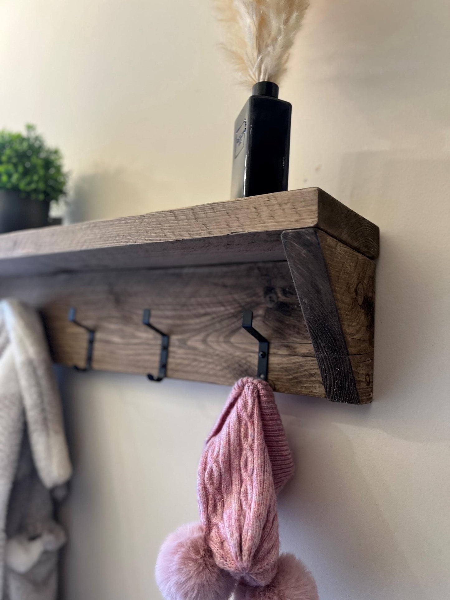 Wooden shelf with hooks on a wall, holding a pink knitted item and a black bottle.