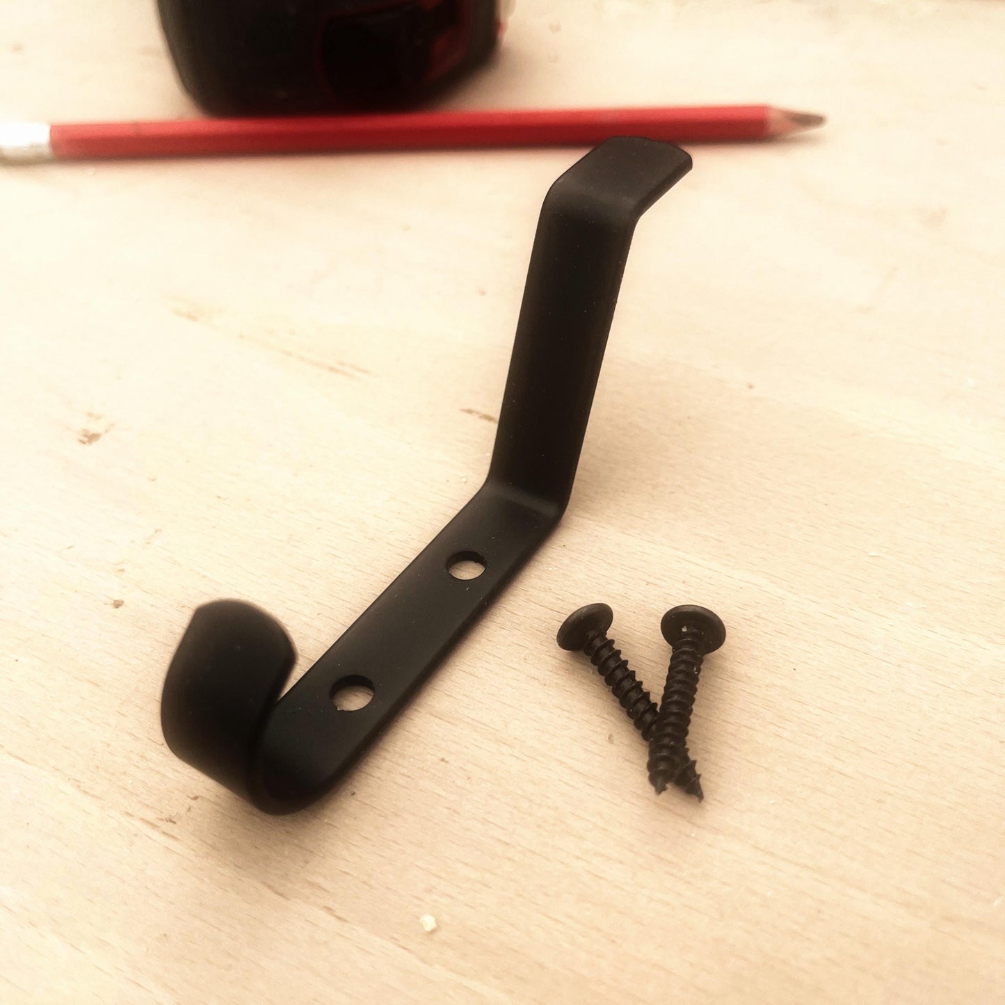 Black metal bracket with two screws on a light wooden surface.