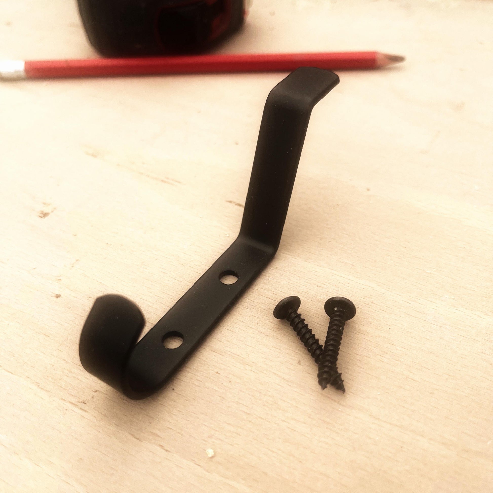 Black metal bracket with two screws on a light wooden surface.