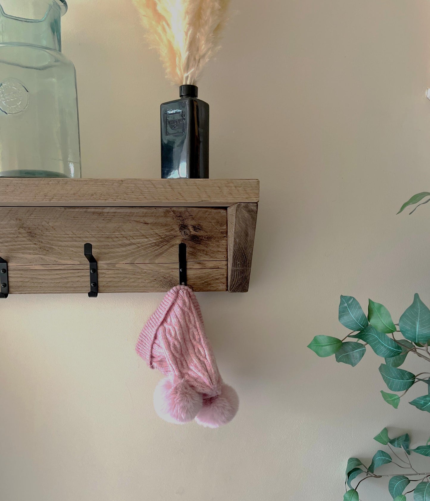 Wooden shelf with hooks on a wall, featuring a pink knitted item and decorative elements.