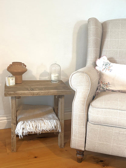 Wooden rustic side table with decorative items next to a grey armchair.