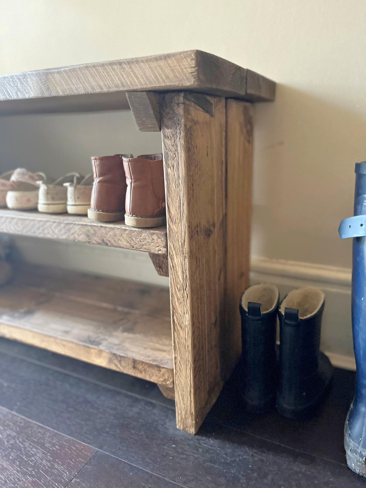 A Rustic wooden shoe rack with shoes and boots on a dark floor.