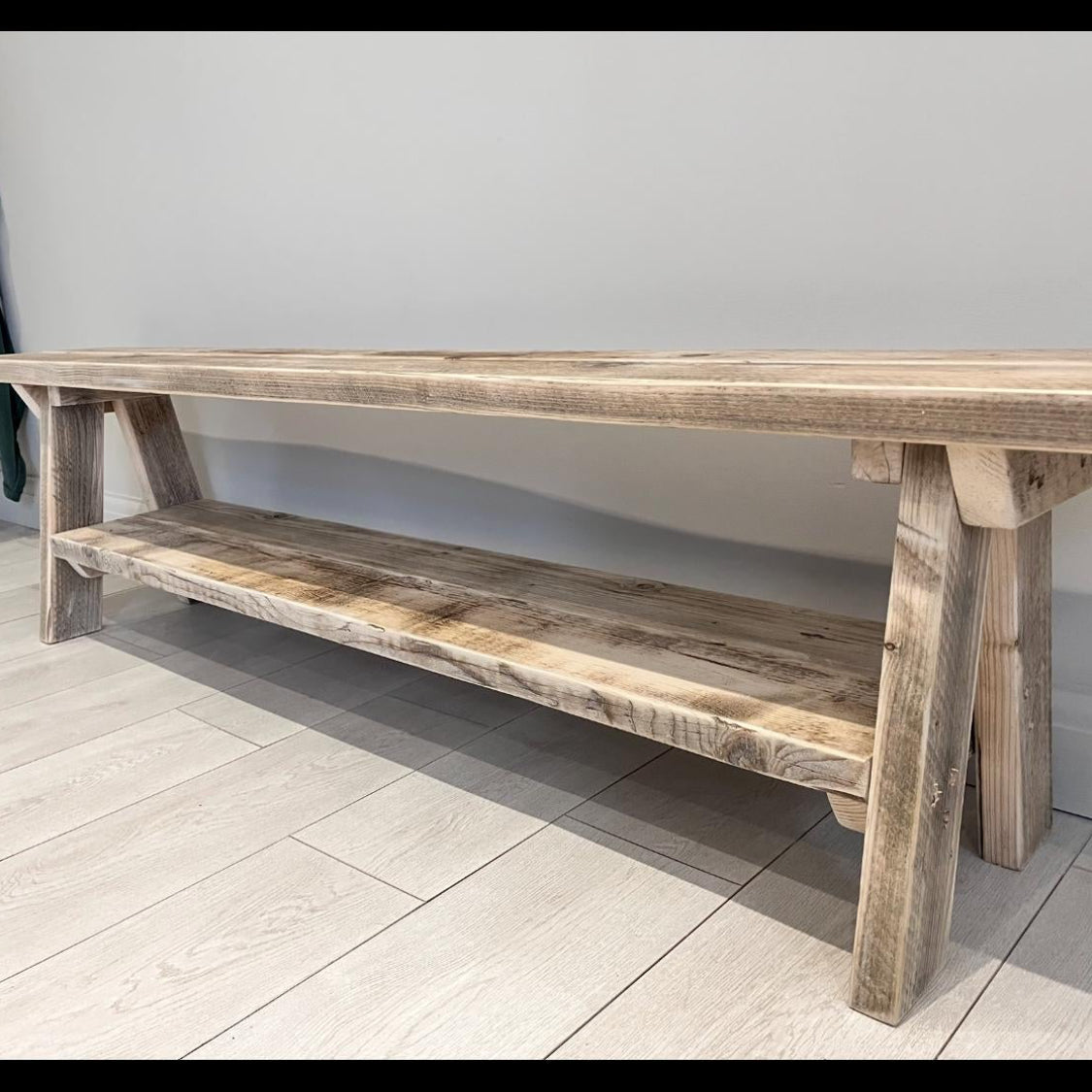 A farmhouse styled, rustic wooden bench with a bottom shelf, in an entryway  setting. (front view)
