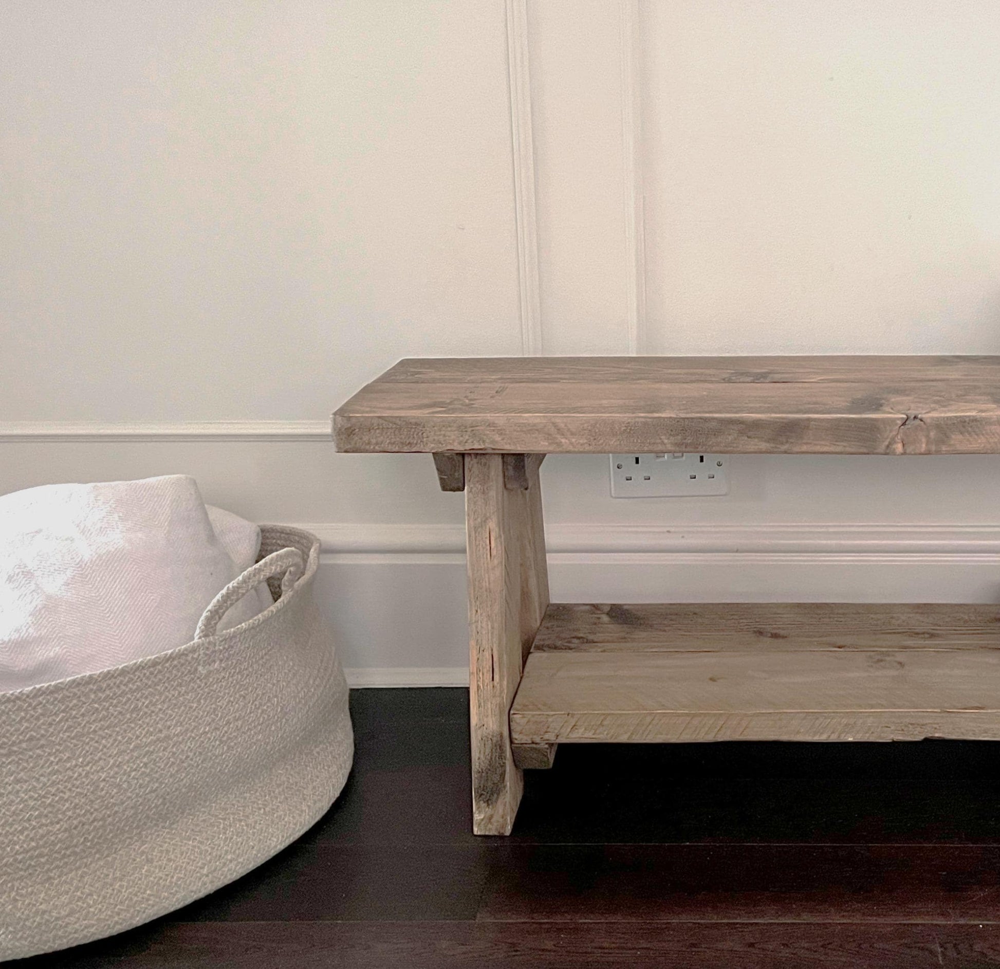 A farmhouse styled, rustic wooden bench with a bottom shelf, in an entryway  setting. (front view)