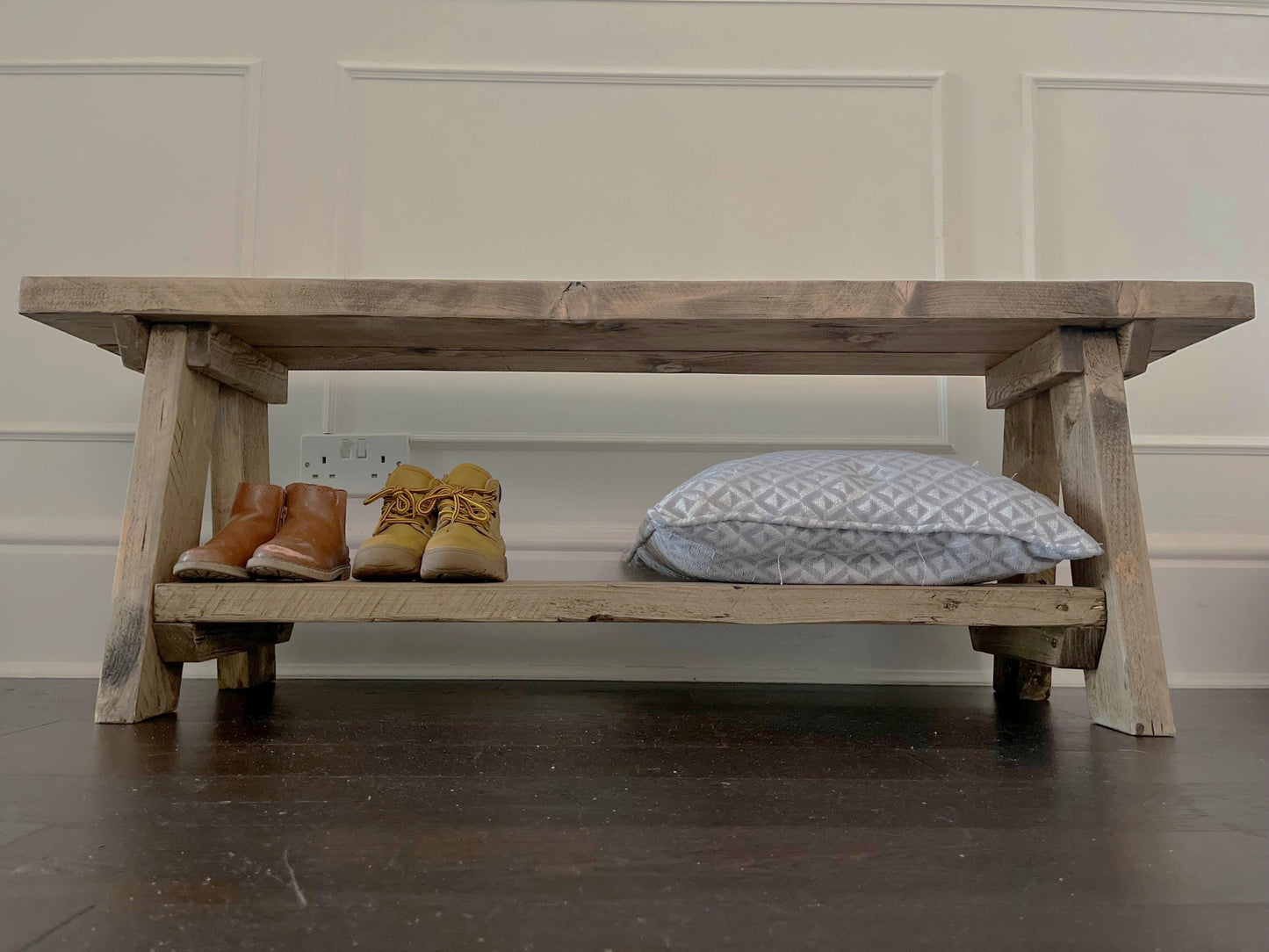 A farmhouse styled, rustic wooden bench with a bottom shelf, in an entryway  setting. (front view)