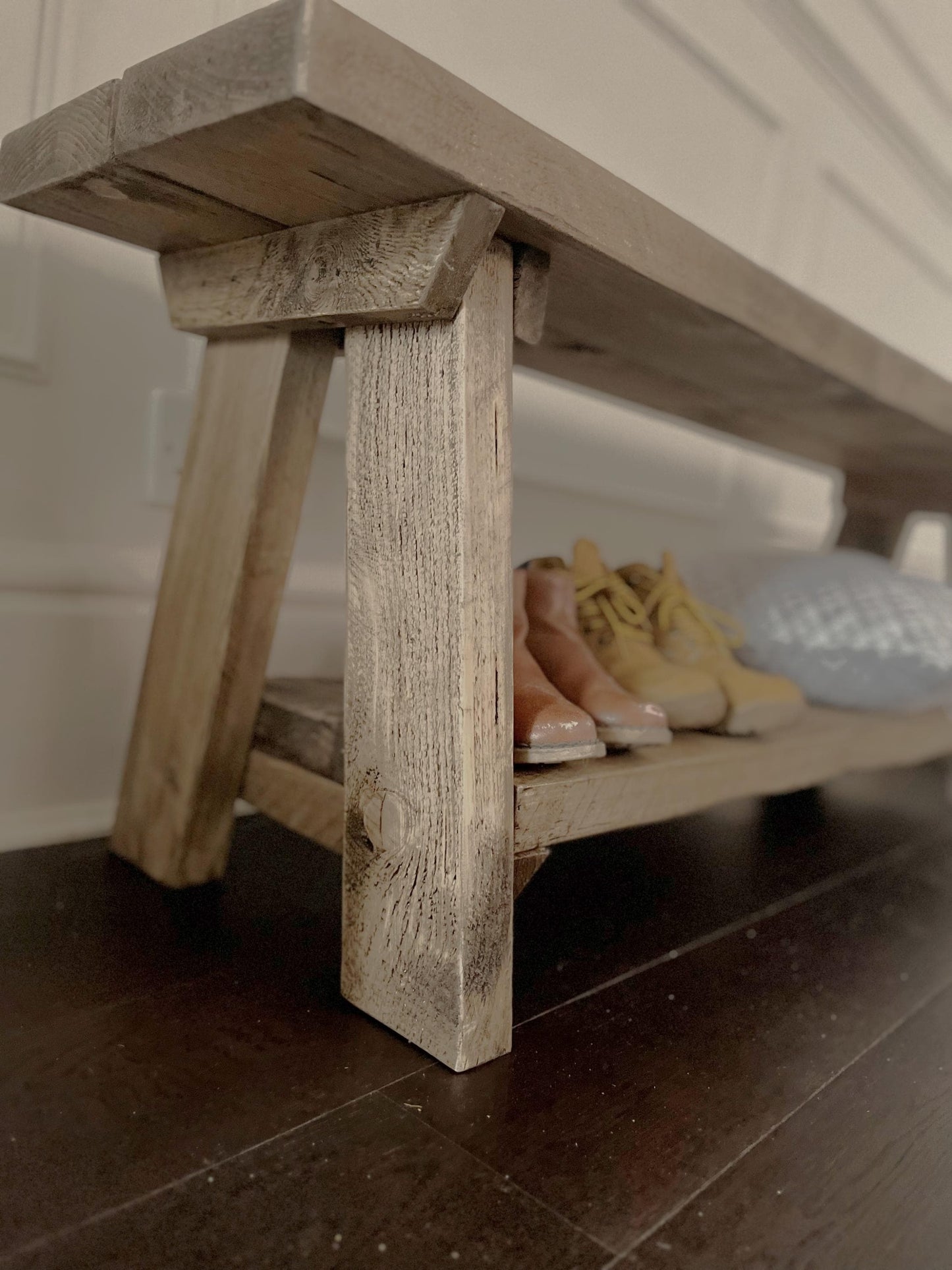 A farmhouse styled, rustic wooden bench with a bottom shelf, in an entryway  setting. (front view)