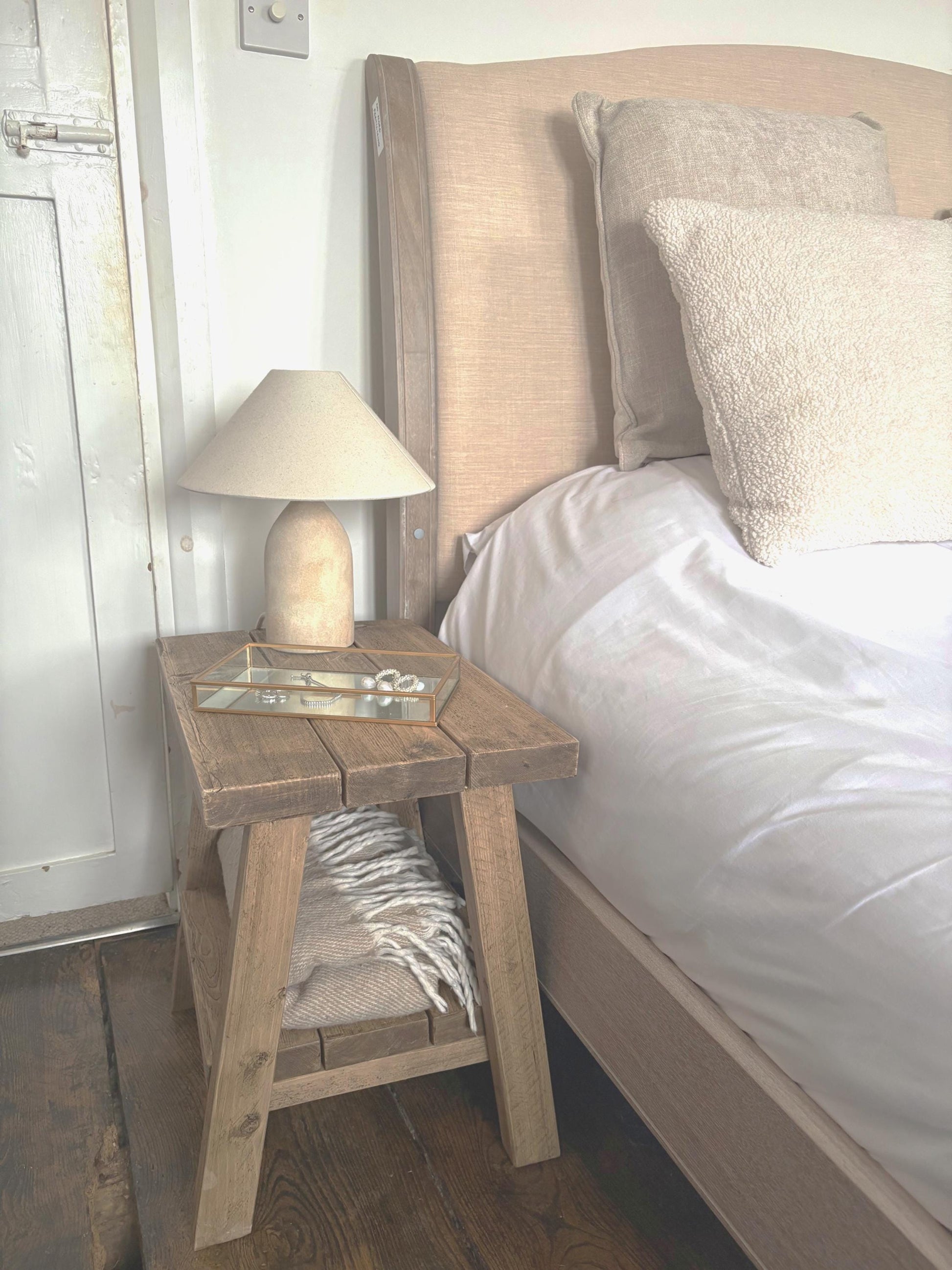 Wooden rustic nightstand with lamp next to a bed in a bedroom setting