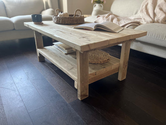 A farmhouse styled, rustic wooden coffee table with decorative items in a living room setting, with a lower shelf. 
