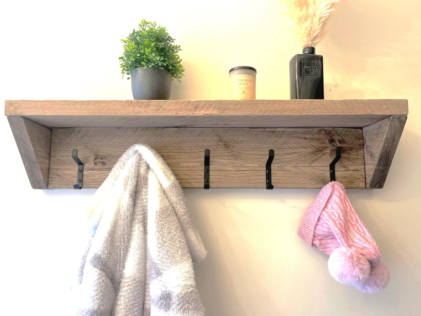 Farmhouse style wooden shelf with hooks holding a towel and pink item against a neutral background (front view)