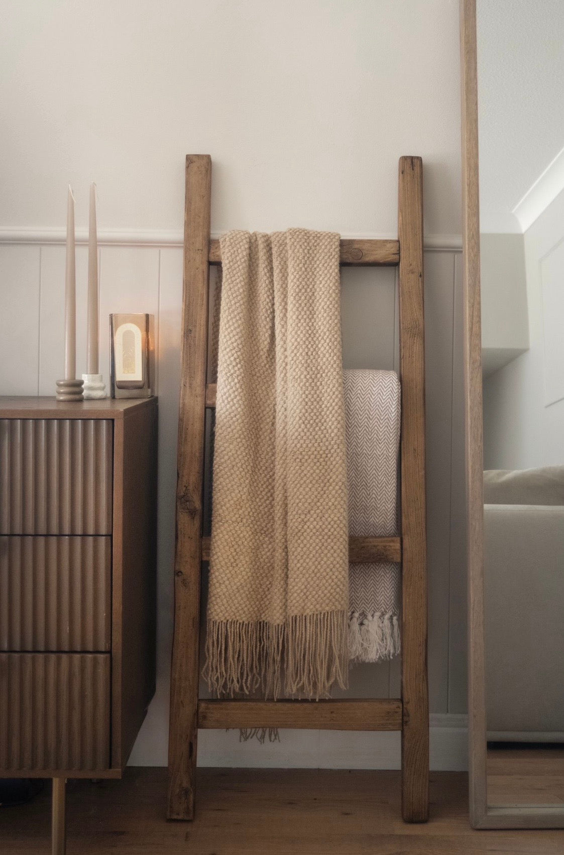 Wooden ladder with a beige blanket against a neutral wall.