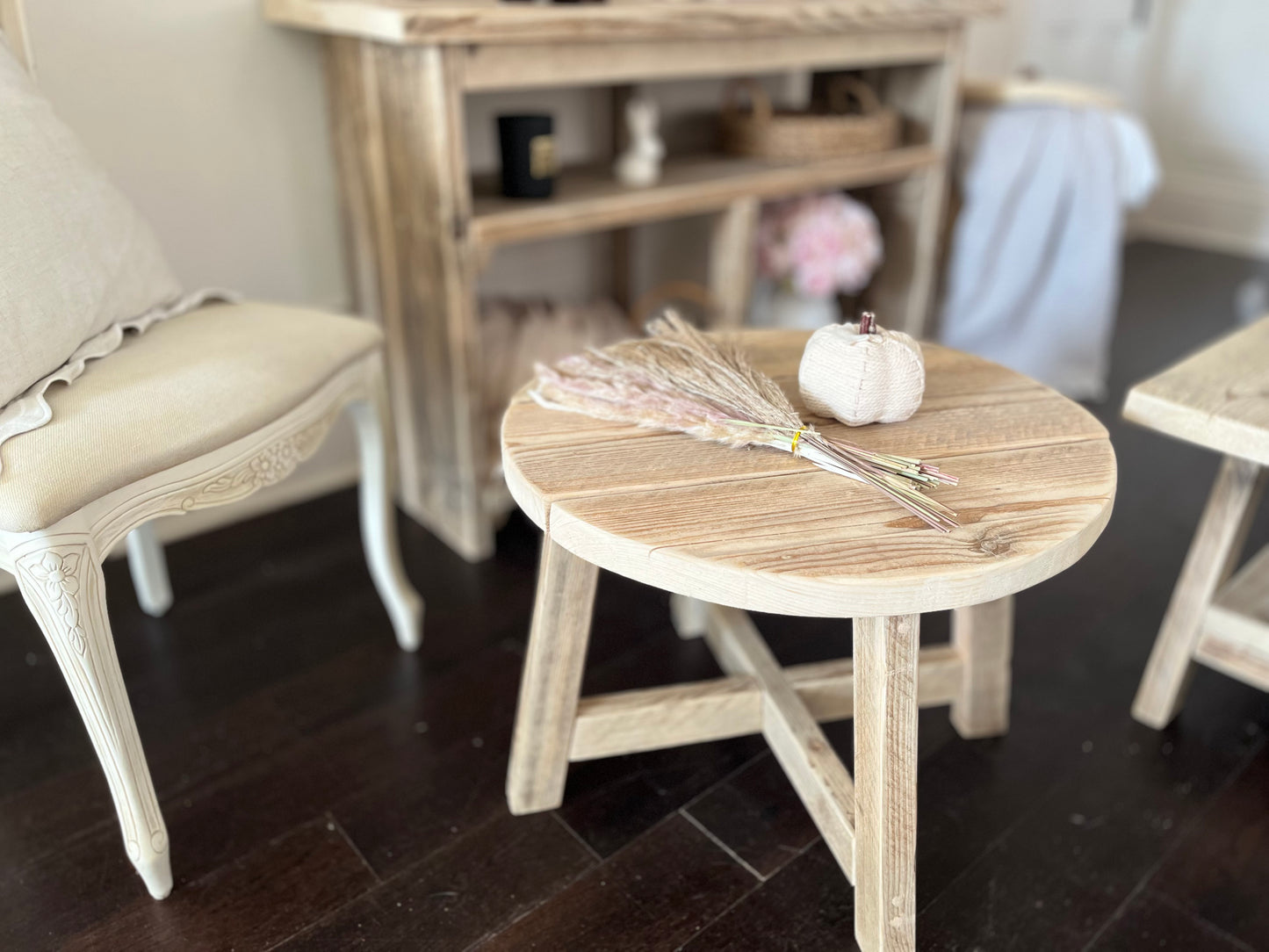 Round wooden table with decorative items in a room with chairs and a shelf.