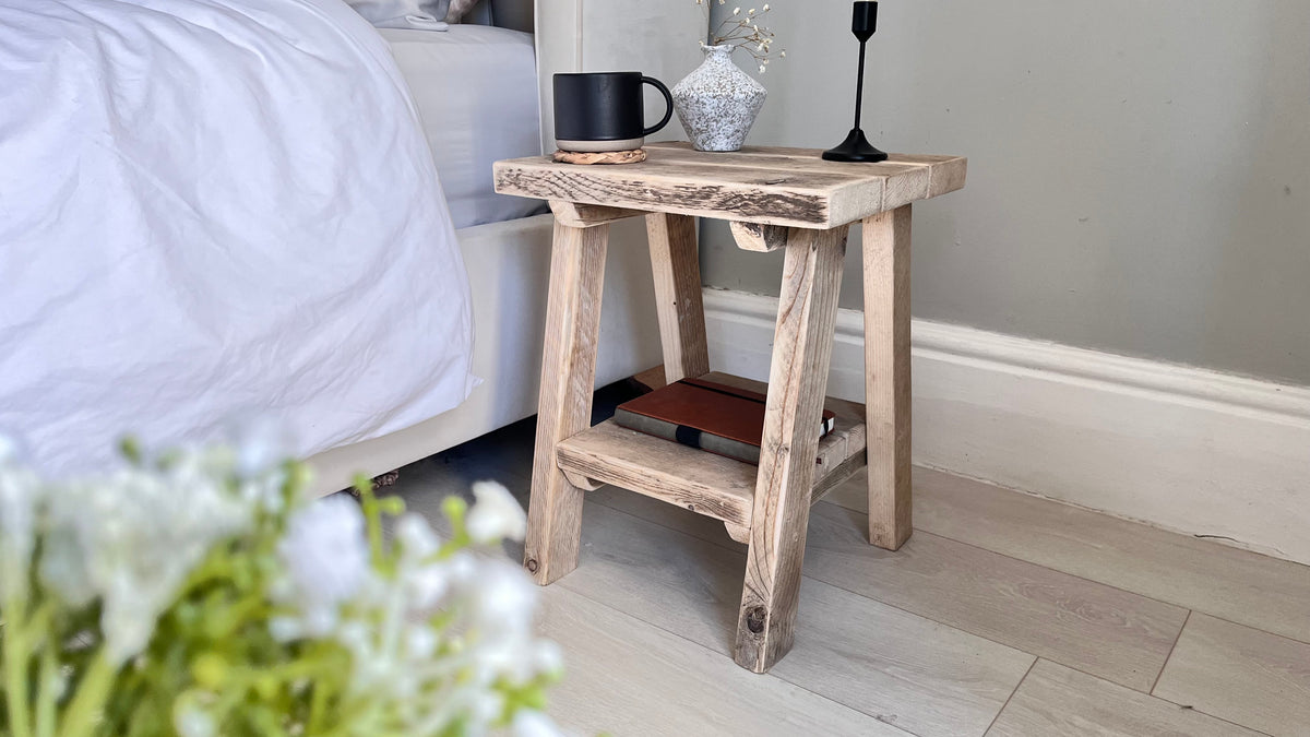 Wooden side table next to a bed with a cup and decorative items.