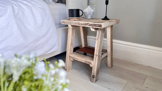 Wooden side table next to a bed with a cup and decorative items.