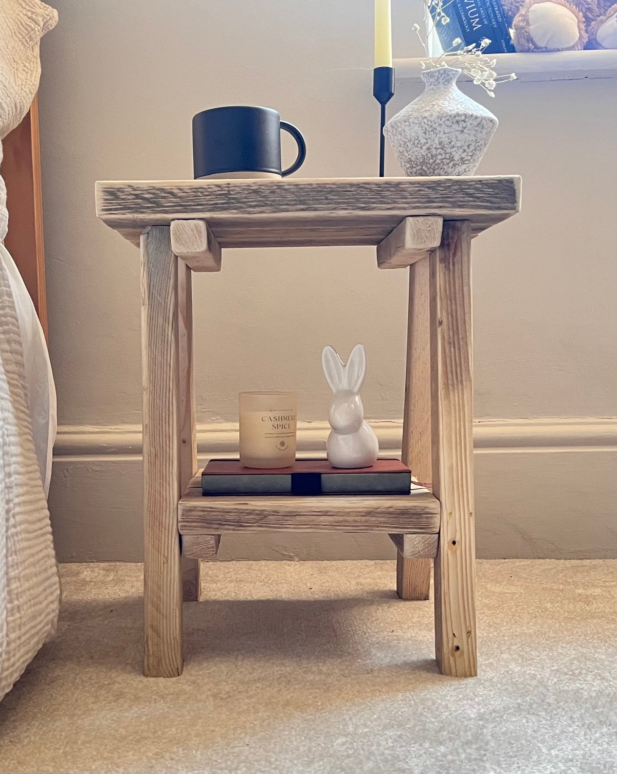 Wooden side table with decorative items including a mug, candle, and rabbit figurine.