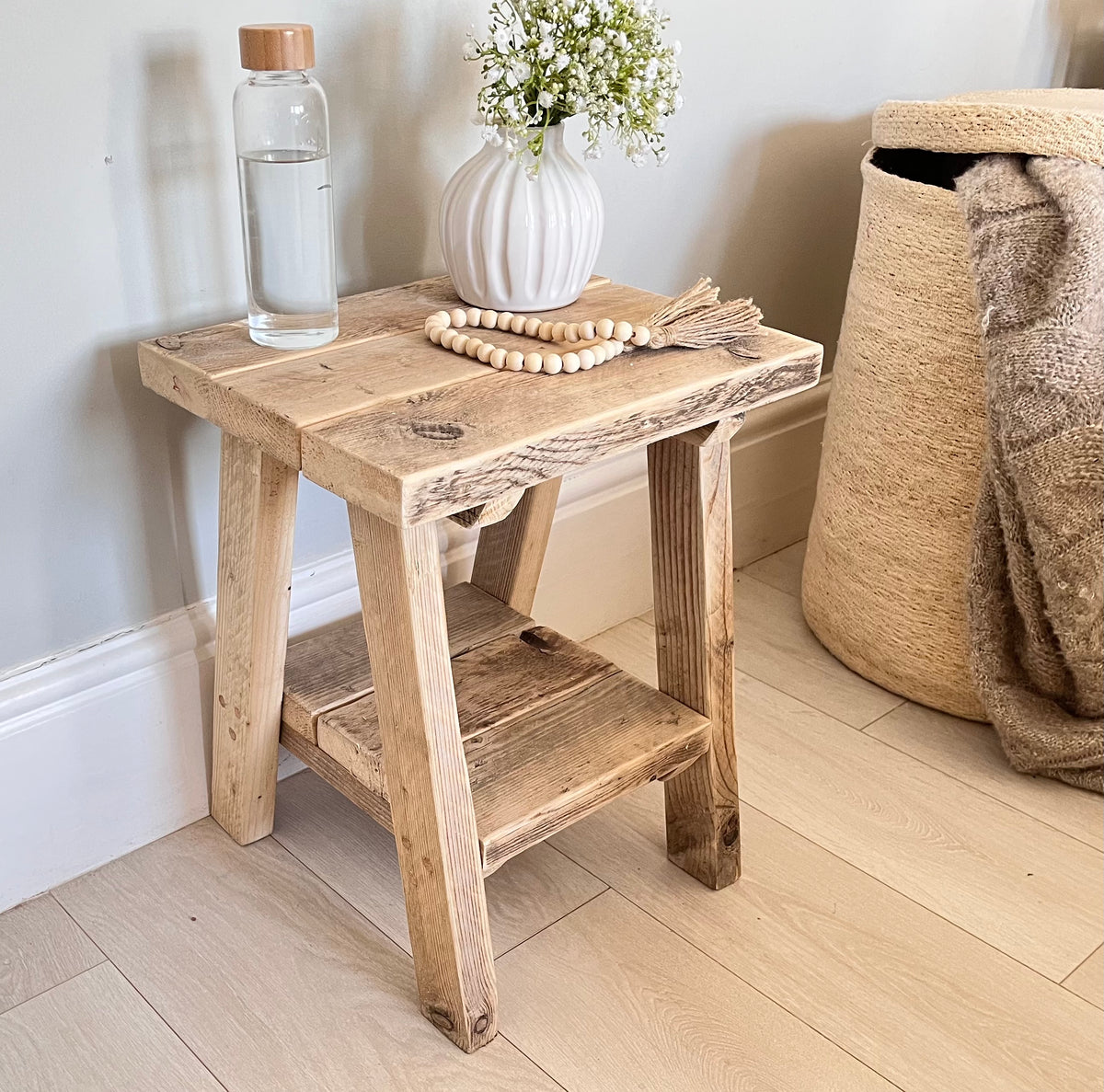 Wooden stool with a vase, water bottle, and decorative items against a light blue wall.