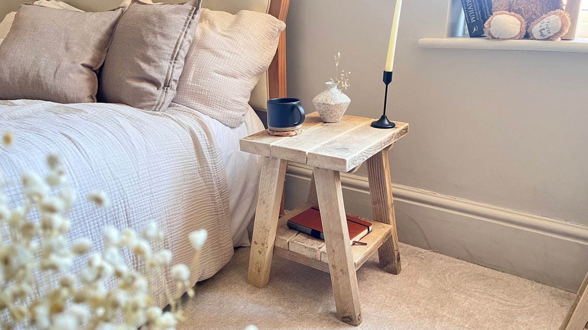 Bedroom with a wooden nightstand next to a bed with pillows and a blue mug.