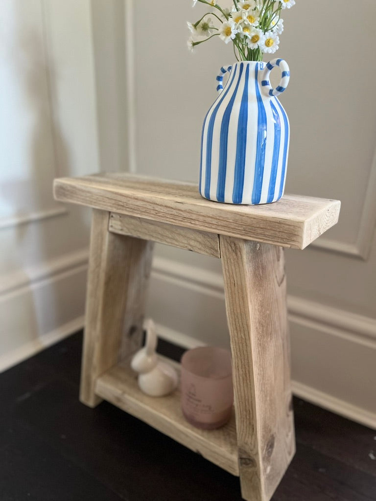 Wooden stool with a blue and white striped vase and flowers on a neutral background
