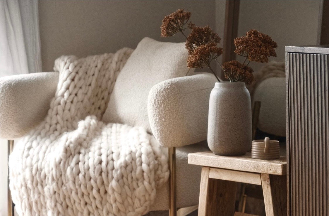 Cozy living room with a textured armchair, decorative vase, and soft lighting.