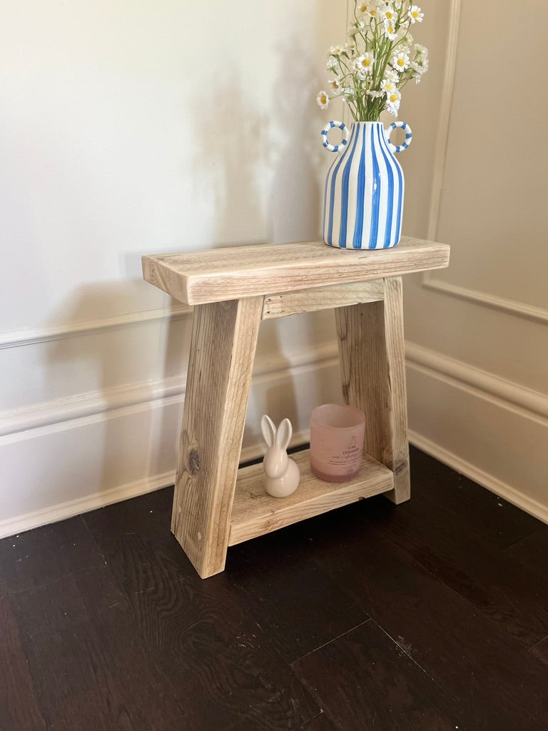 Wooden side table with a blue and white striped vase and decorative items against a wall.