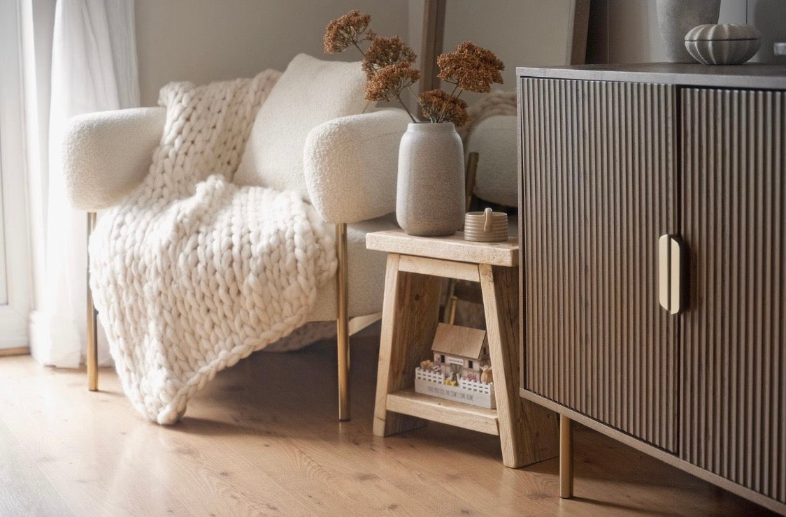 Living room with a white armchair, wooden side table, and striped cabinet.