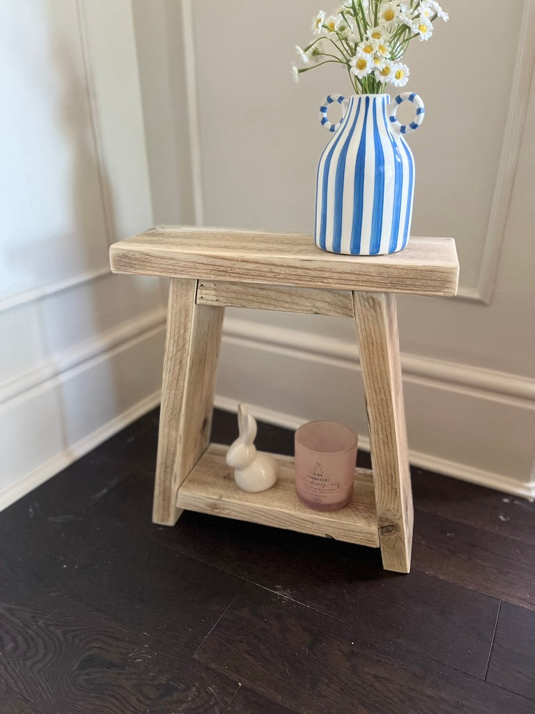 Wooden side table with a blue and white striped vase and flowers on a dark wooden floor.