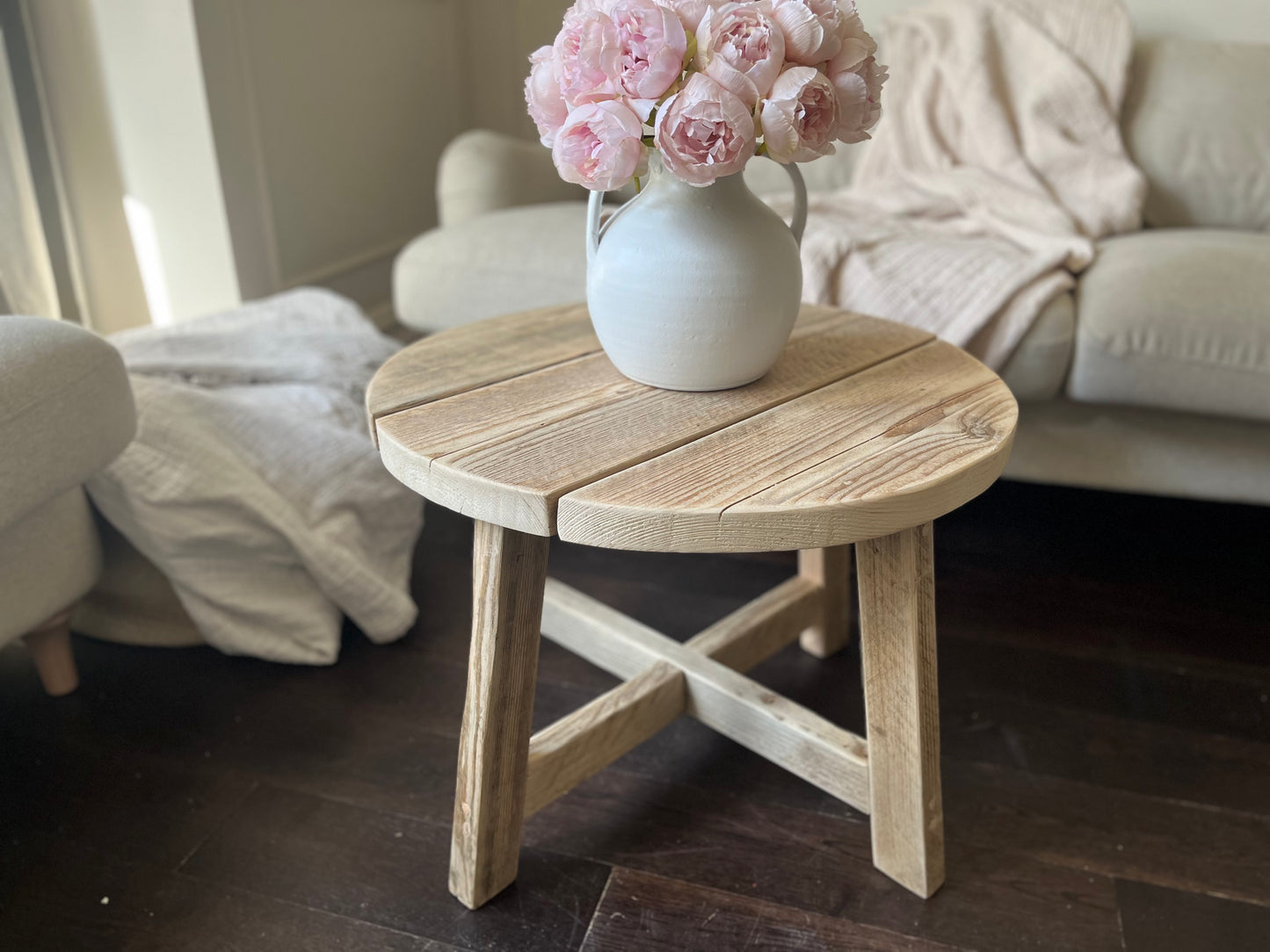 Wooden side table with a vase of pink flowers in a living room setting