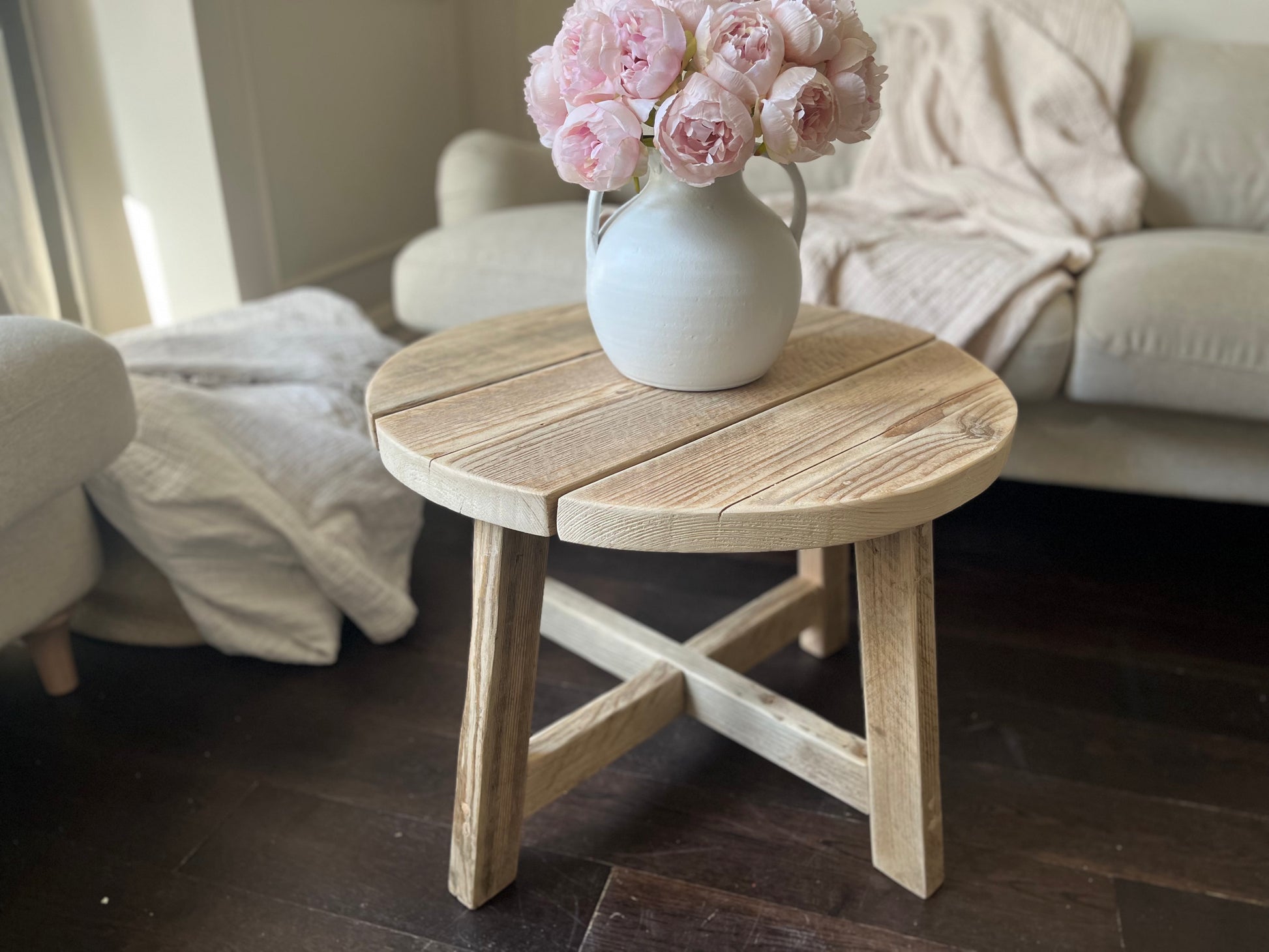 Wooden side table with a vase of pink flowers in a living room setting