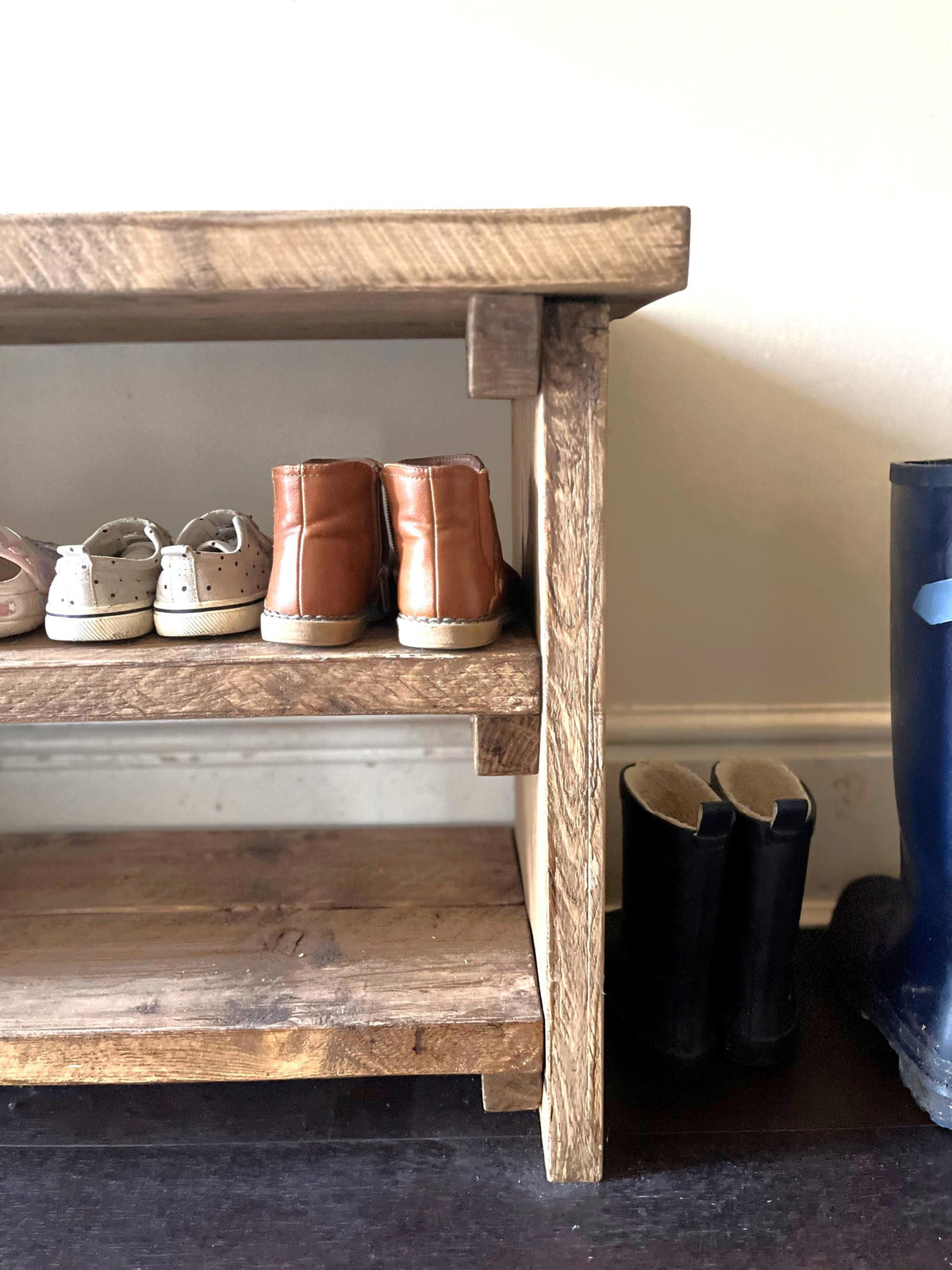 Wooden shoe rack with shoes and boots on a plain background