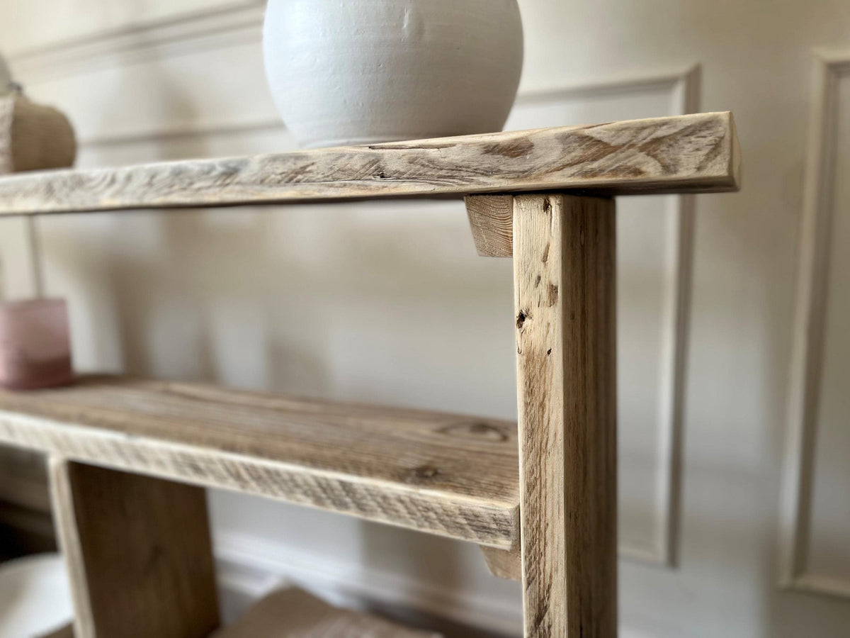Close up of a farmhouse style wooden slim console table with one long shelf and two lower bottom shelves, in a living room setting (front view)