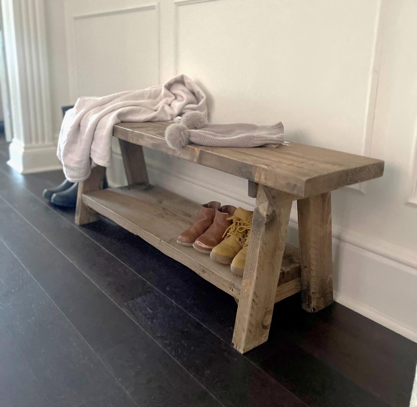 A farmhouse styled, rustic wooden bench with a bottom shelf, in an entryway  setting. (front view)