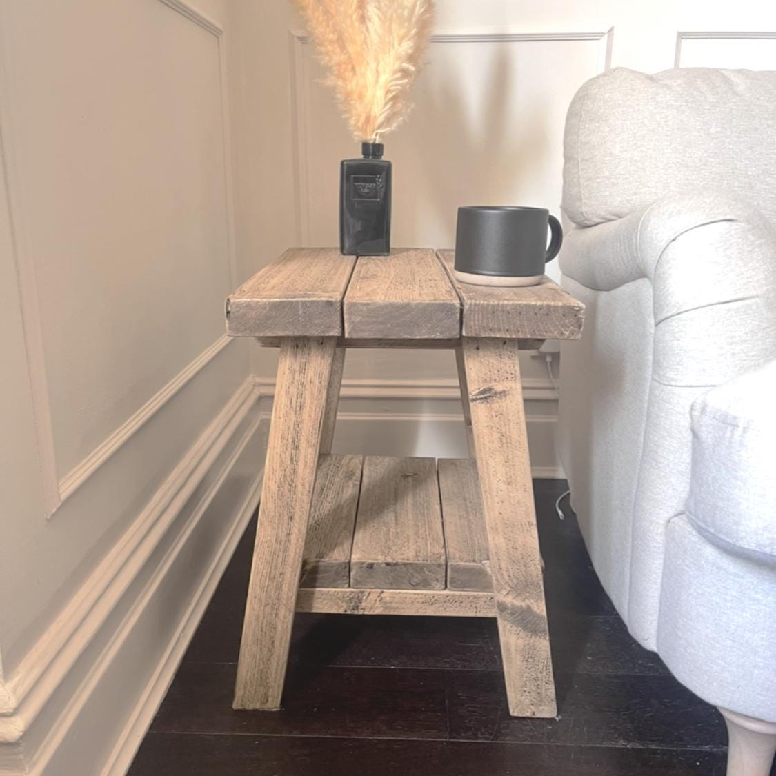 Wooden rustic side table with a black mug and decorative vase against a white wall.