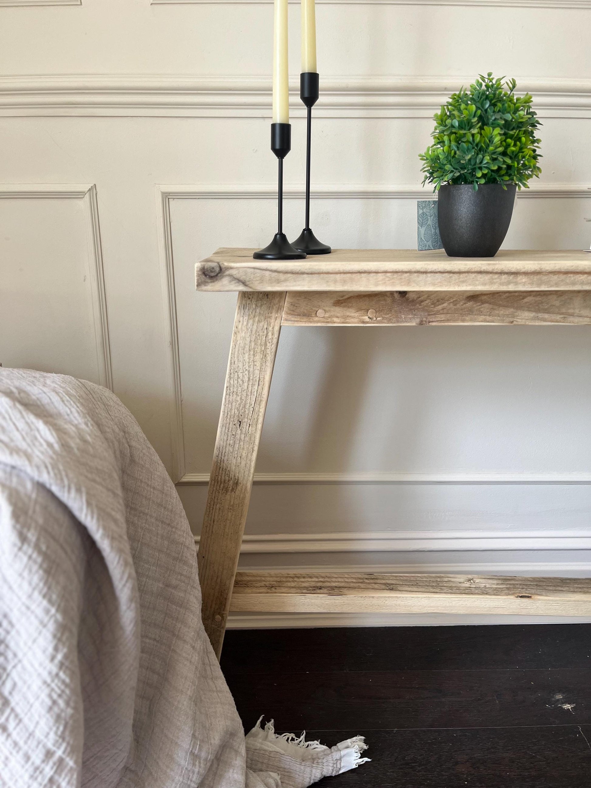 Wooden console table with a plant and candles against a neutral wall.
