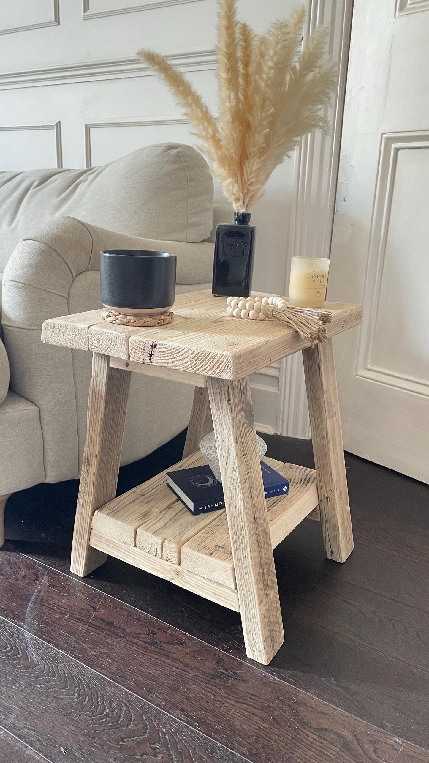 A farmhouse style wooden side table with a bottom shelf, in a living room setting (side view)