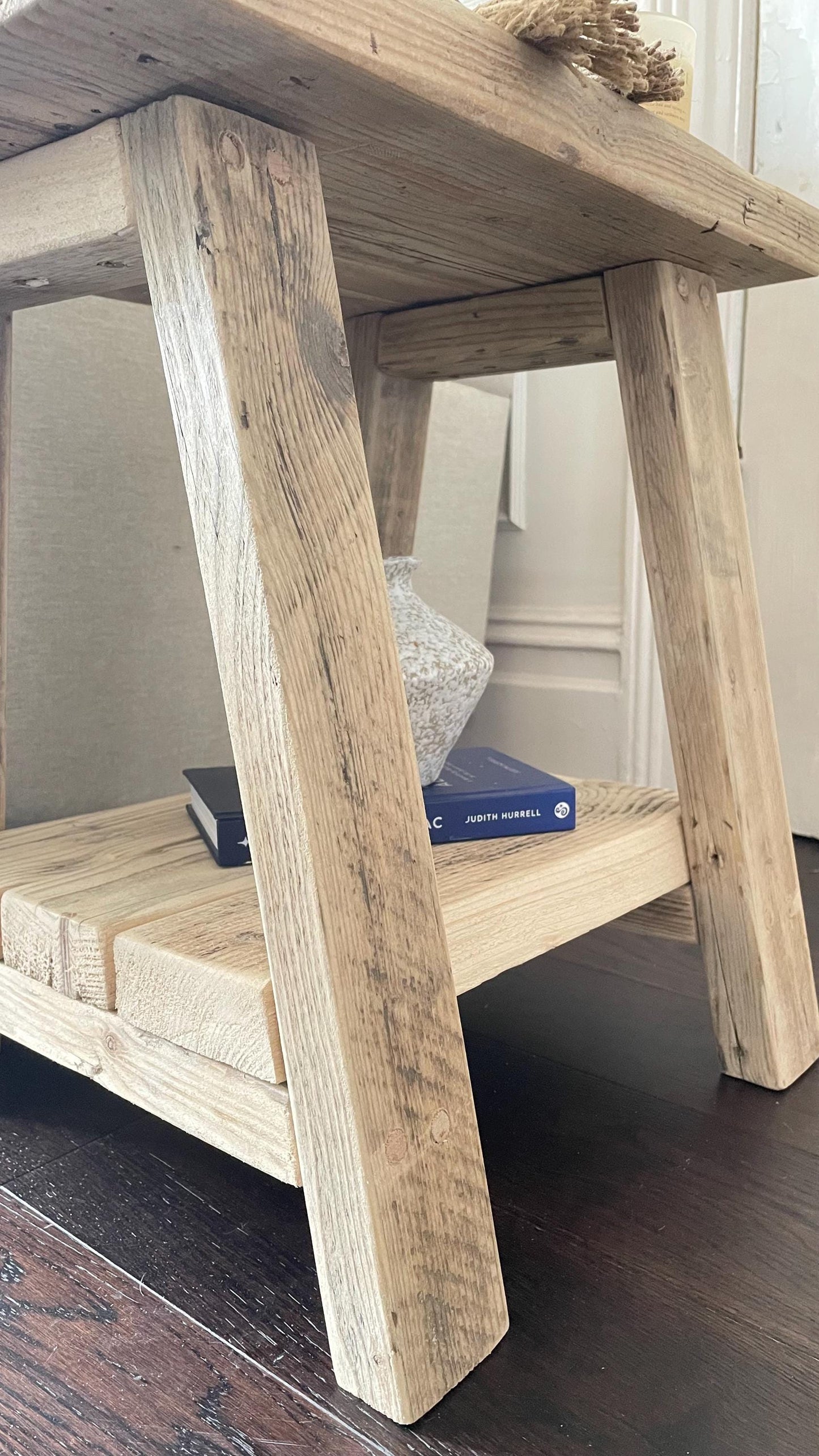 Wooden side table with a rustic design and a bottom shelf on a dark wooden floor.