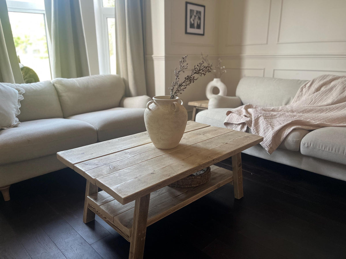A farmhouse style rustic wooden coffee table with a bottom shelf, in a living room setting (front view)