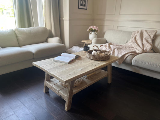 A farmhouse style rustic wooden coffee table with a bottom shelf, in a living room setting (front view)