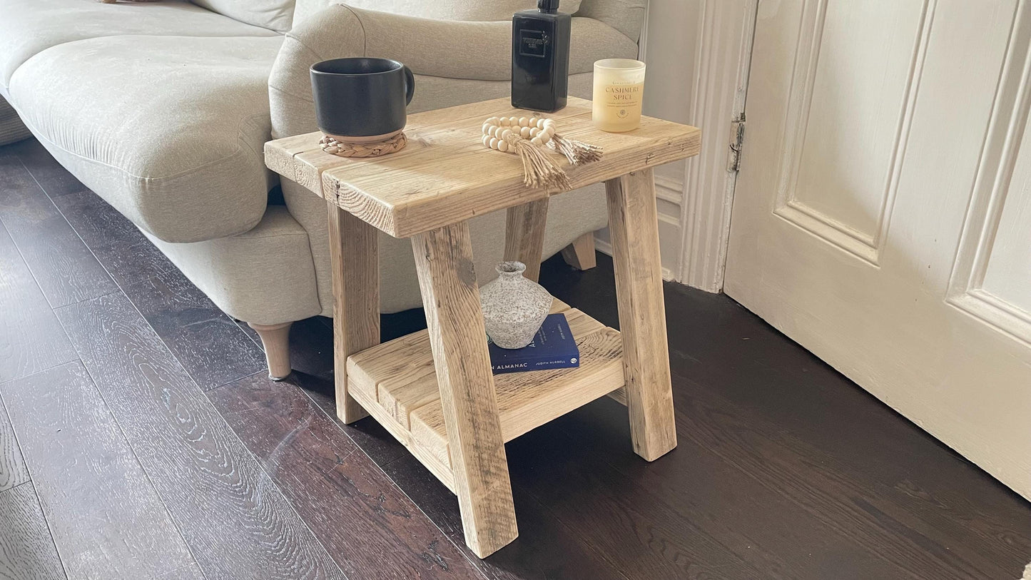 A farmhouse style wooden side table with a bottom shelf, in a living room setting (front view)