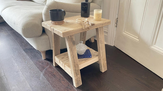 A farmhouse style wooden side table with a bottom shelf, in a living room setting (front view)