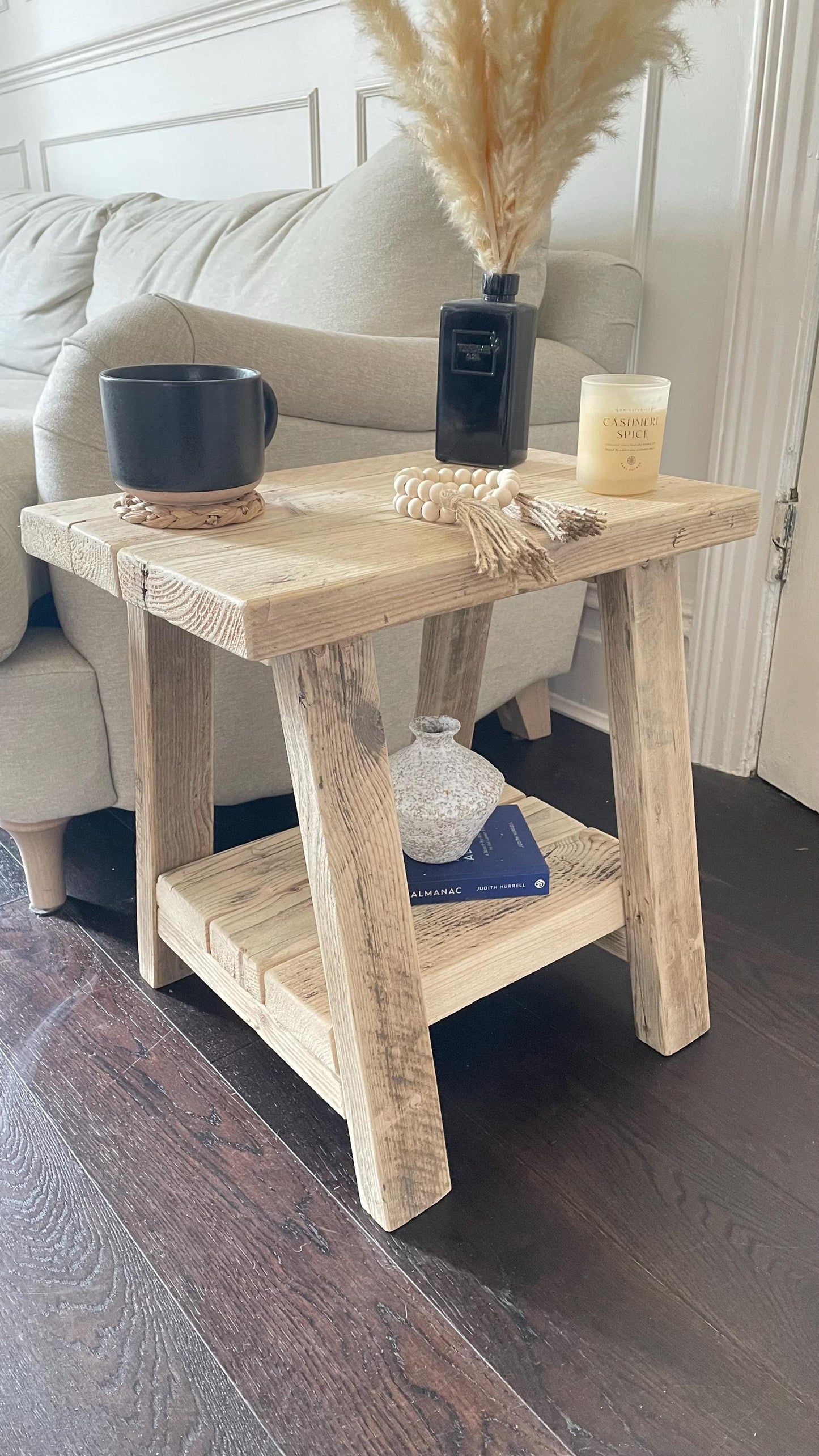 A farmhouse style wooden side table with a bottom shelf, in a living room setting (front view)