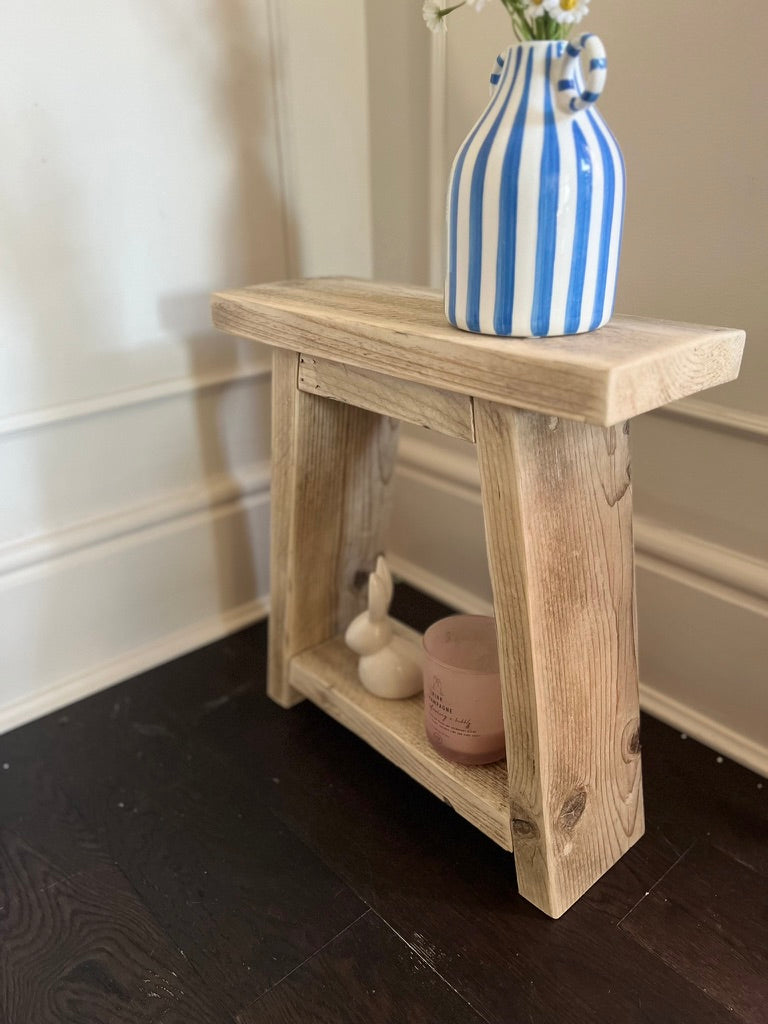 Wooden side table with a blue and white striped vase on a dark wooden floor.