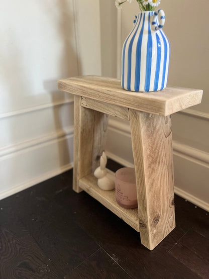 Wooden side table with a blue and white striped vase on a dark wooden floor.